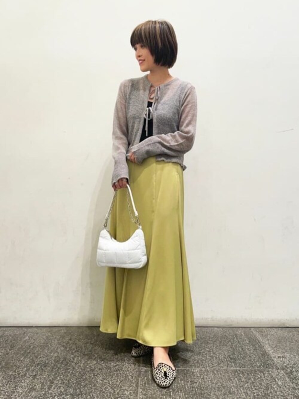 グレー系のカーディガン/ボレロ、イエロー系のスカート、ホワイト系のビジネスバッグを着用したレディースの秋コーディネートの1枚目の写真