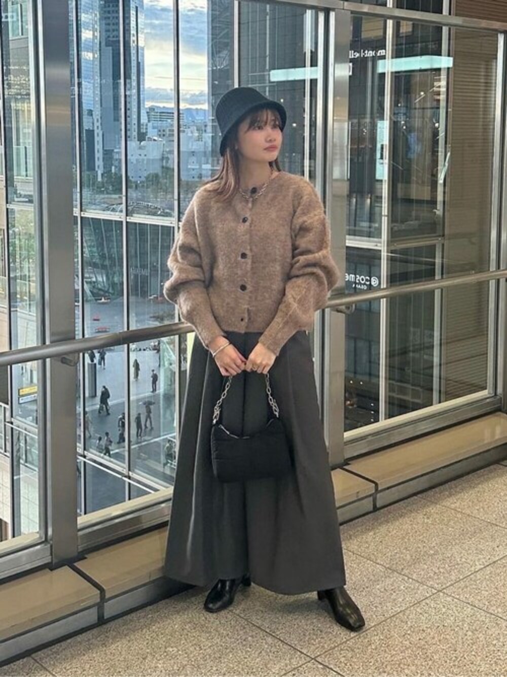 ブラウン系のカーディガン/ボレロ、グレー系のスラックス、ブラック系のビジネスバッグを着用したレディースの秋コーディネートの1枚目の写真