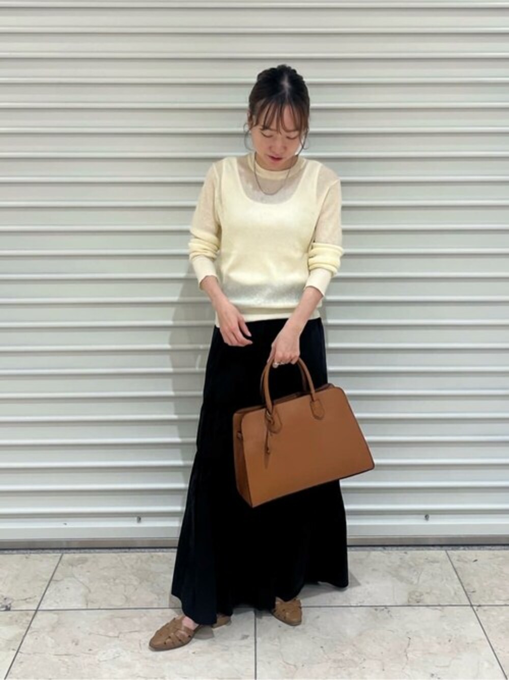 ベージュ系のニット/セーター、ブラック系のスカート、イエロー系のビジネスバッグを着用したレディースの秋コーディネートの1枚目の写真