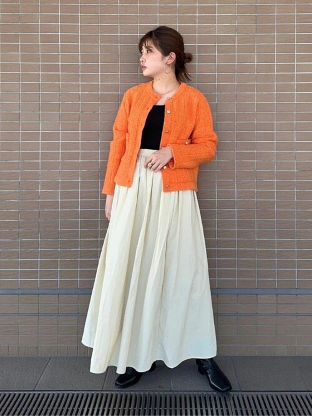 オレンジ系のカーディガン/ボレロ、ベージュ系のスカート、ブラック系のニット/セーターを着用したレディースの秋コーディネートの1枚目の写真
