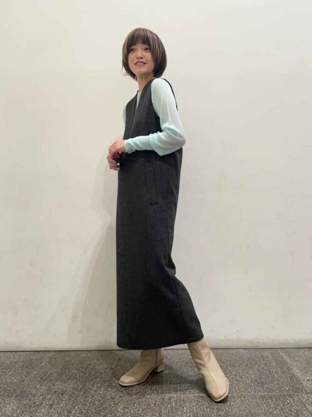 グレー系のジャンパースカート、ブルー系のニット/セーター、ベージュ系のブーツを着用したレディースの秋コーディネートの1枚目の写真