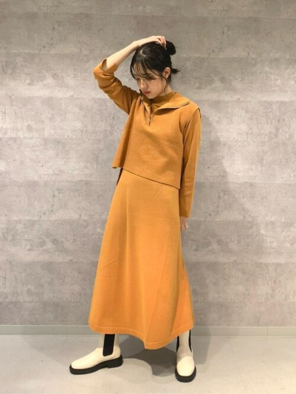 オレンジ系のワンピース、ホワイト系のブーツ、グレー系のベストを着用したレディースの秋コーディネートの1枚目の写真