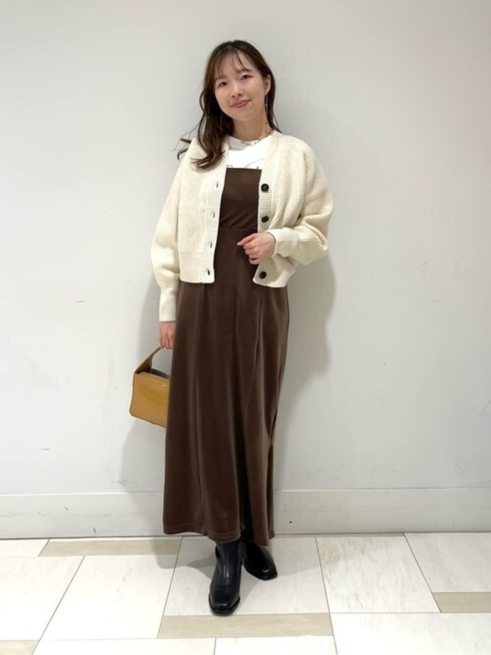 ブラウン系のワンピース、ホワイト系のカーディガン/ボレロ、ベージュ系のビジネスバッグを着用したレディースの秋コーディネートの1枚目の写真