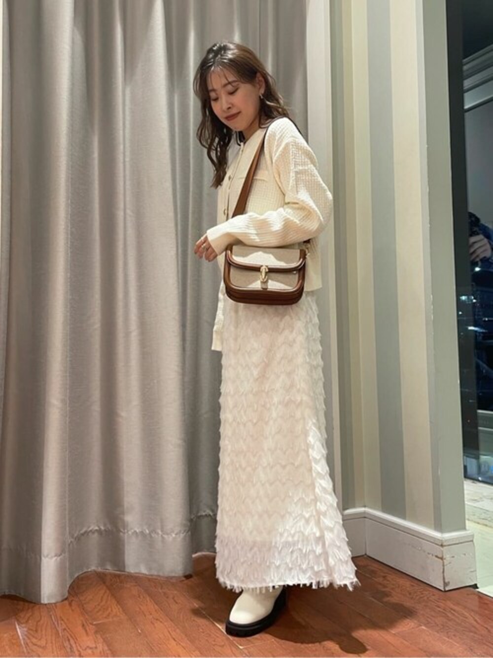 ベージュ系のスカート、ホワイト系のブーツ、ブラウン系のビジネスバッグを着用したレディースの秋コーディネートの1枚目の写真