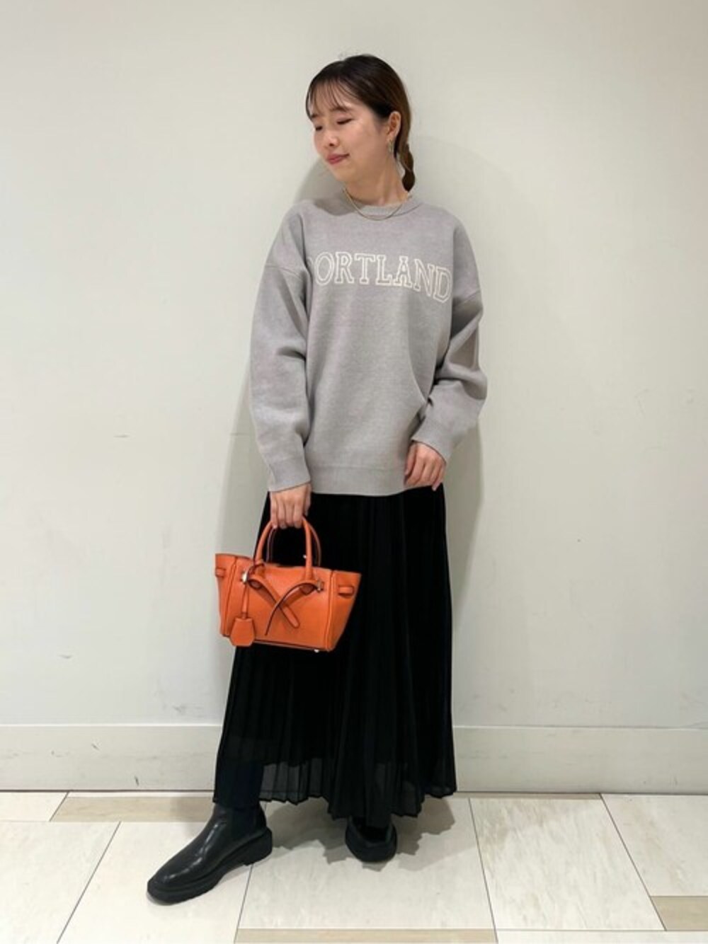 グレー系のニット/セーター、ブラック系のスカート、オレンジ系のビジネスバッグを着用したレディースの秋コーディネートの1枚目の写真
