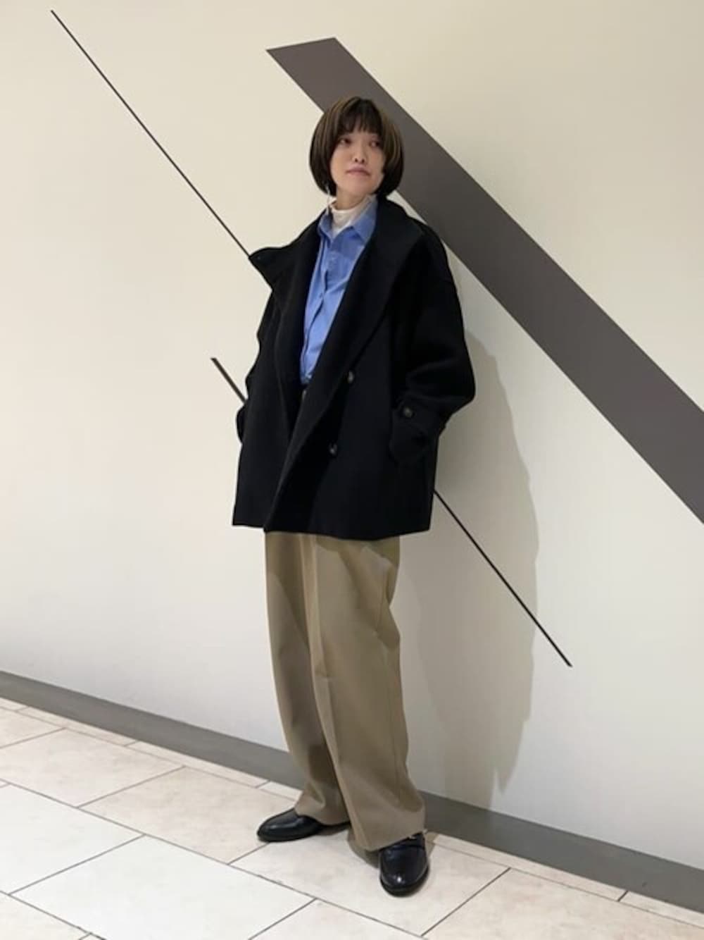 ブラック系のステンカラーコート、ホワイト系のTシャツ/カットソー、ブルー系のシャツ/ブラウスを着用したレディースの秋コーディネートの1枚目の写真