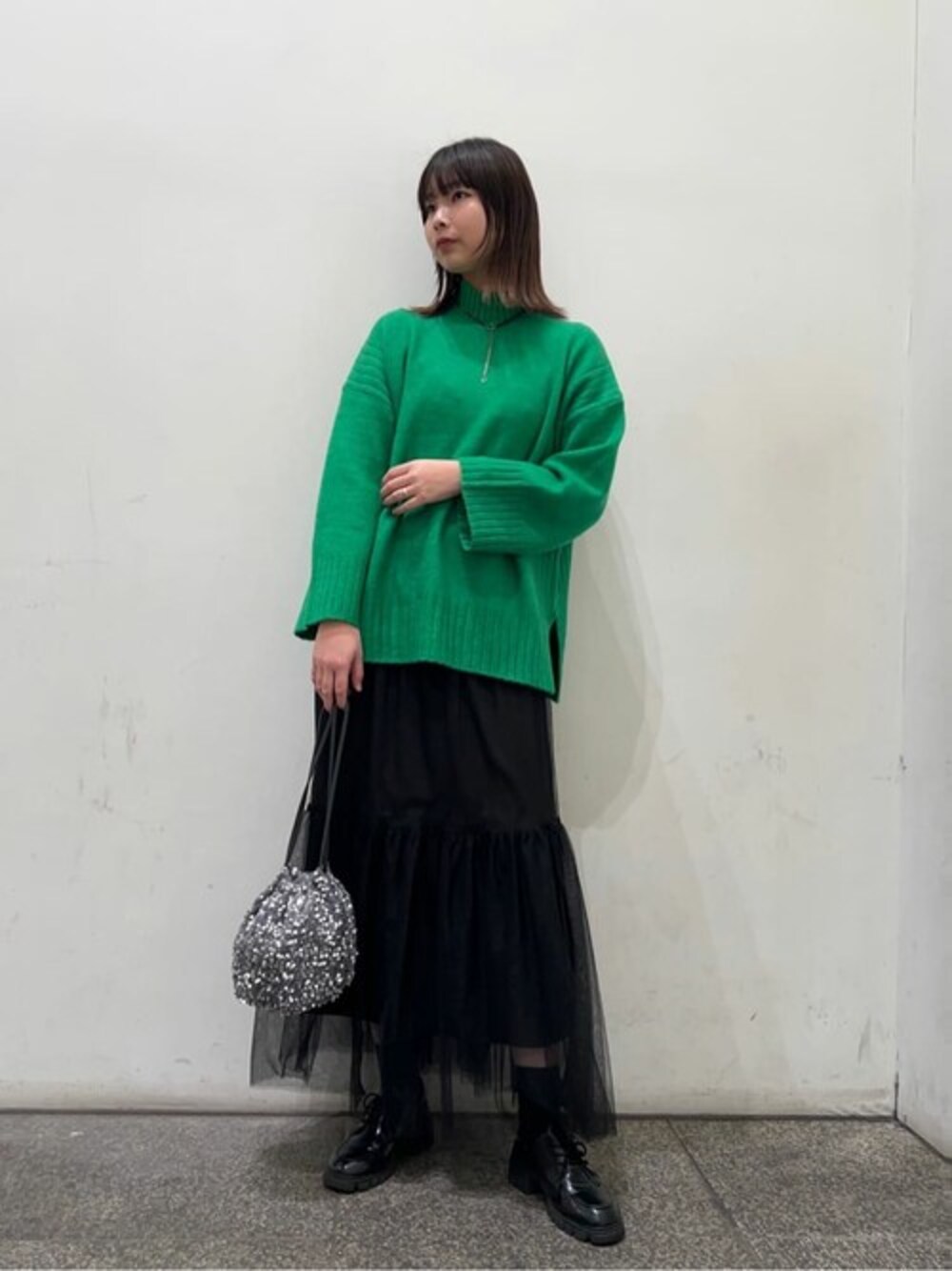 グリーン系のニット/セーター、ブラック系のスカート、グレー系のビジネスバッグを着用したレディースの秋コーディネートの1枚目の写真