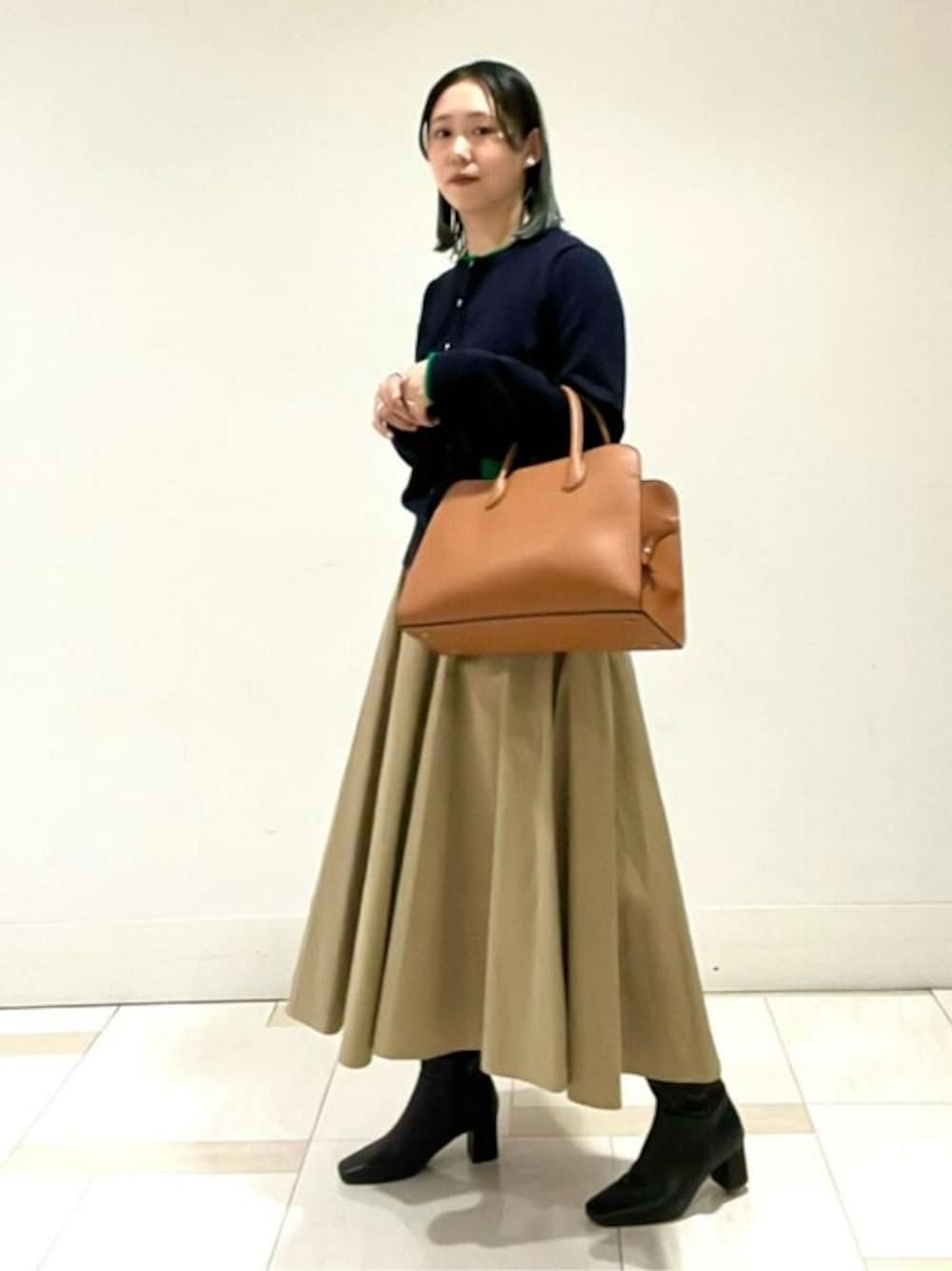 ブルー系のカーディガン/ボレロ、ベージュ系のスカート、イエロー系のビジネスバッグを着用したレディースの冬コーディネートの1枚目の写真