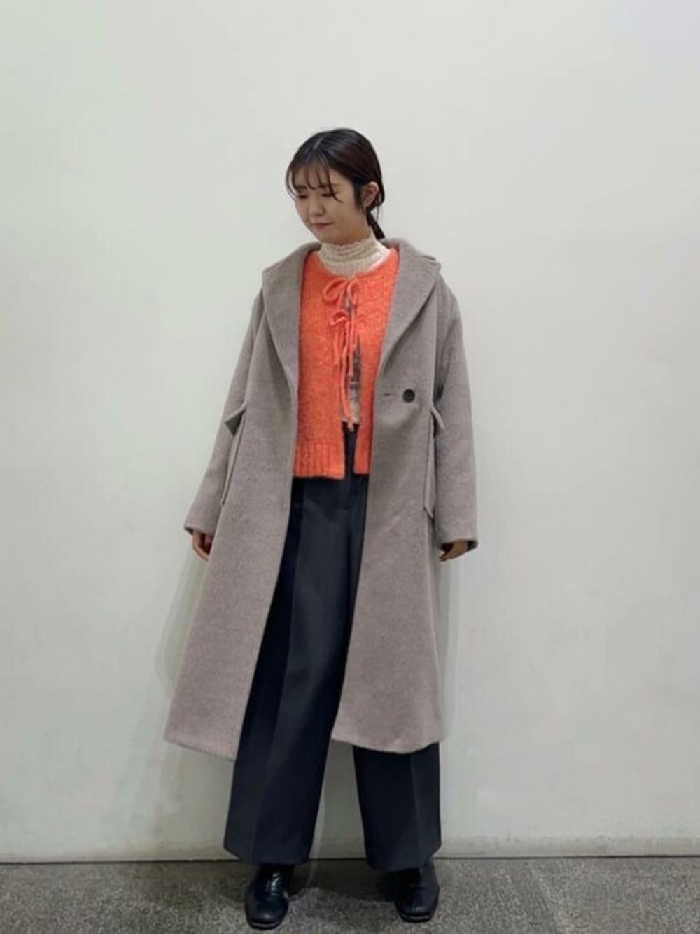 ベージュ系のチェスターコート、オレンジ系のカーディガン/ボレロ、ブラック系のブーツを着用したレディースの冬コーディネートの1枚目の写真