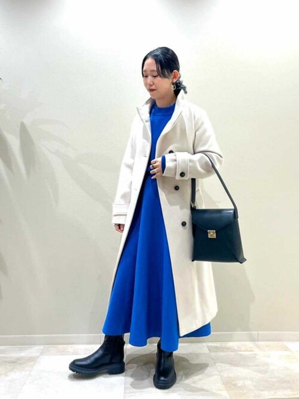 ホワイト系のステンカラーコート、ブラック系のブーツ、ブラック系のショルダーバッグを着用したレディースの冬コーディネートの1枚目の写真