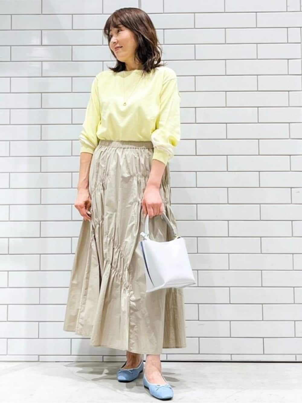 イエロー系のニット/セーター、ベージュ系のスカート、グレー系のショルダーバッグを着用したレディースの春コーディネートの1枚目の写真
