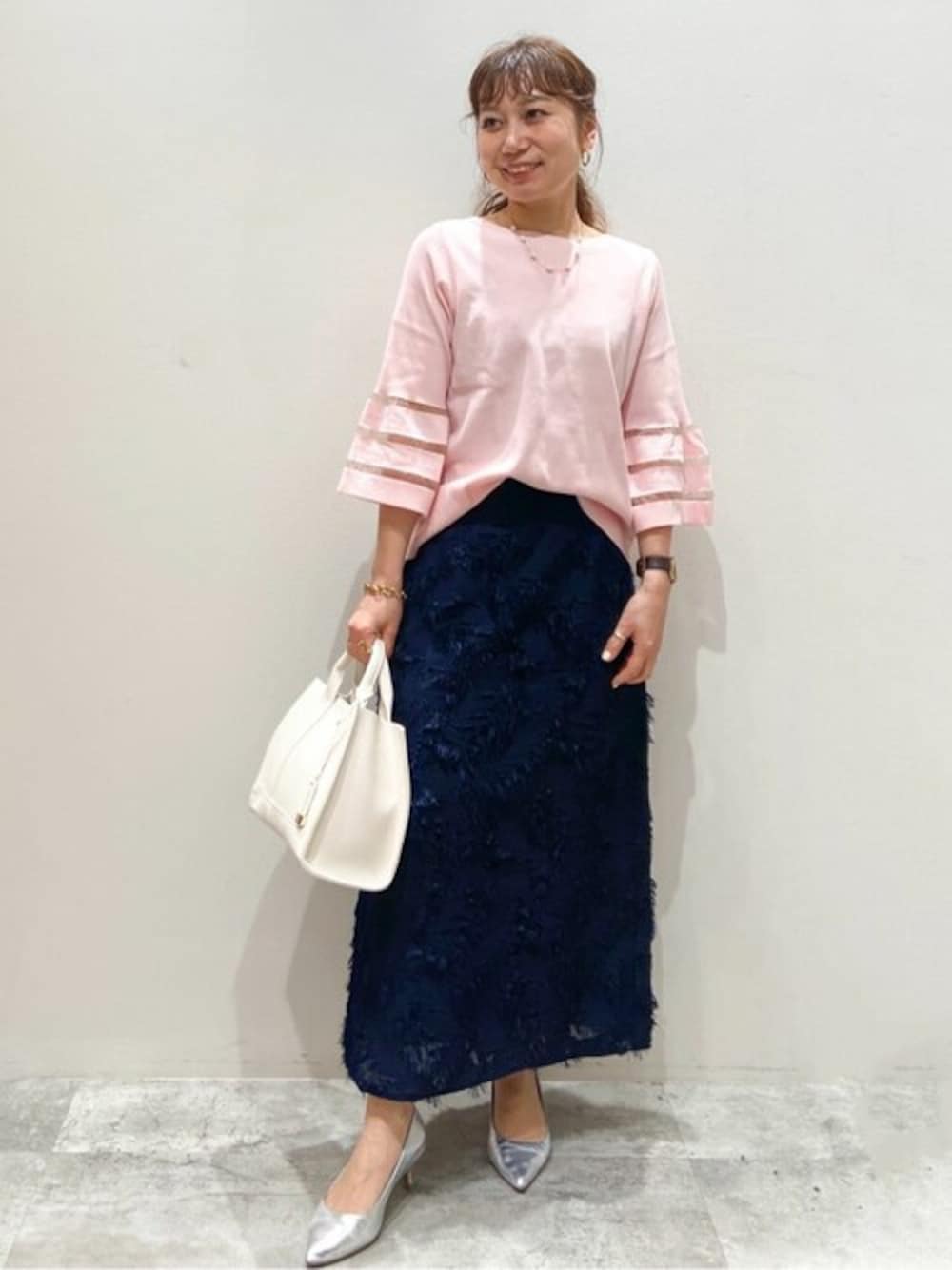 ピンク系のニット/セーター、ブルー系のスカート、ホワイト系のトートバッグを着用したレディースの春コーディネートの1枚目の写真