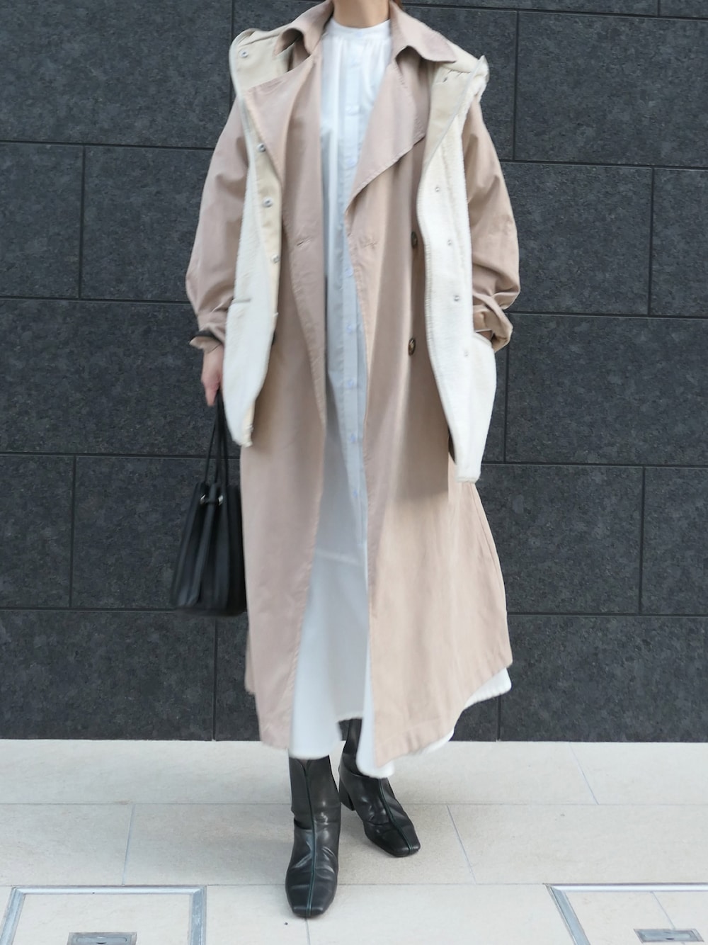 ブラック系のショルダーバッグ、ベージュ系のトレンチコート、ホワイト系のダウンベストを着用したレディースの冬コーディネートの1枚目の写真