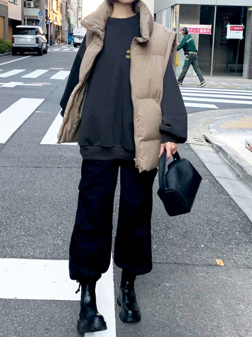 ブラック系のスウェット、ベージュ系のダウンベスト、ブラック系のカーゴパンツを着用したレディースの秋コーディネートの1枚目の写真