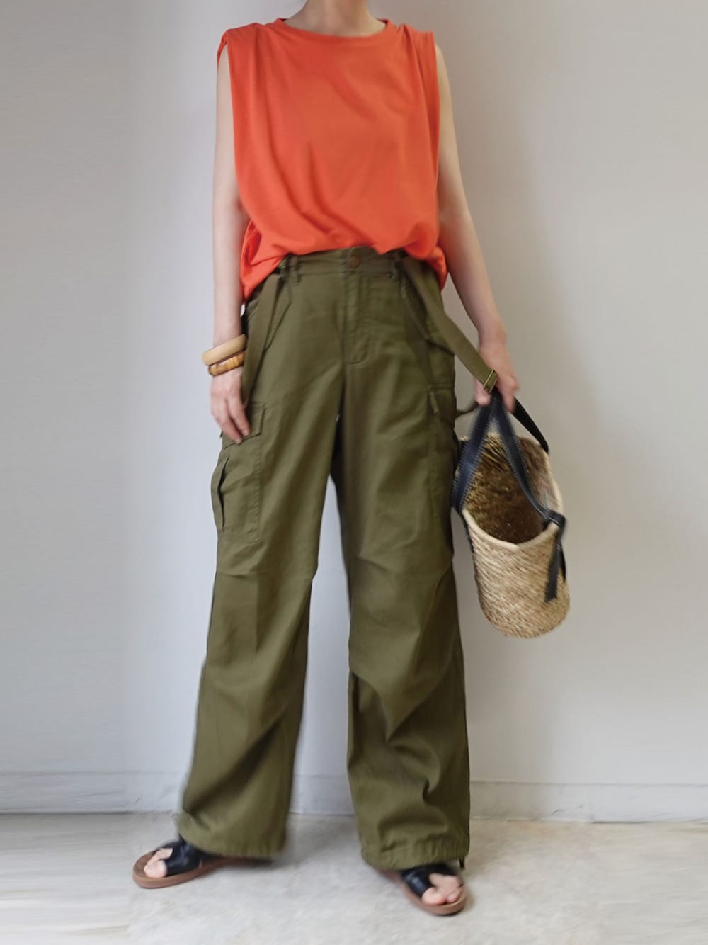 ブラック系のかごバッグ、オレンジ系のタンクトップ、グリーン系のカーゴパンツを着用したレディースの夏コーディネートの1枚目の写真