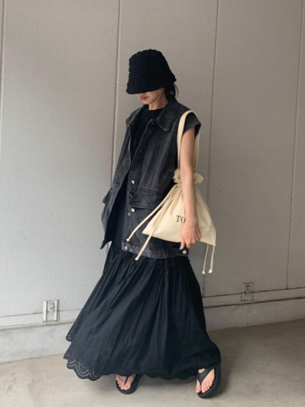 ブラック系のベスト、ブラック系のスカート、ブラック系のサンダルを着用したレディースの夏コーディネートの1枚目の写真