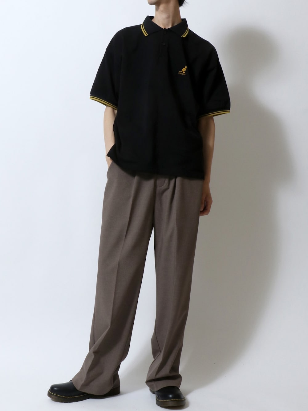 ブラック系のポロシャツ、ブラウン系のスラックス、ブラック系のドレスシューズを着用したメンズの夏コーディネートの1枚目の写真