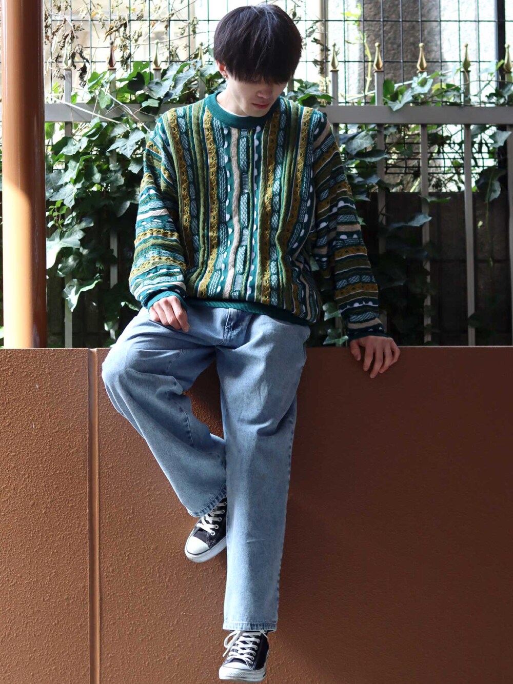 グリーン系のニット/セーター、ブラック系のスニーカー、ブルー系のデニムパンツを着用したメンズの春コーディネートの1枚目の写真