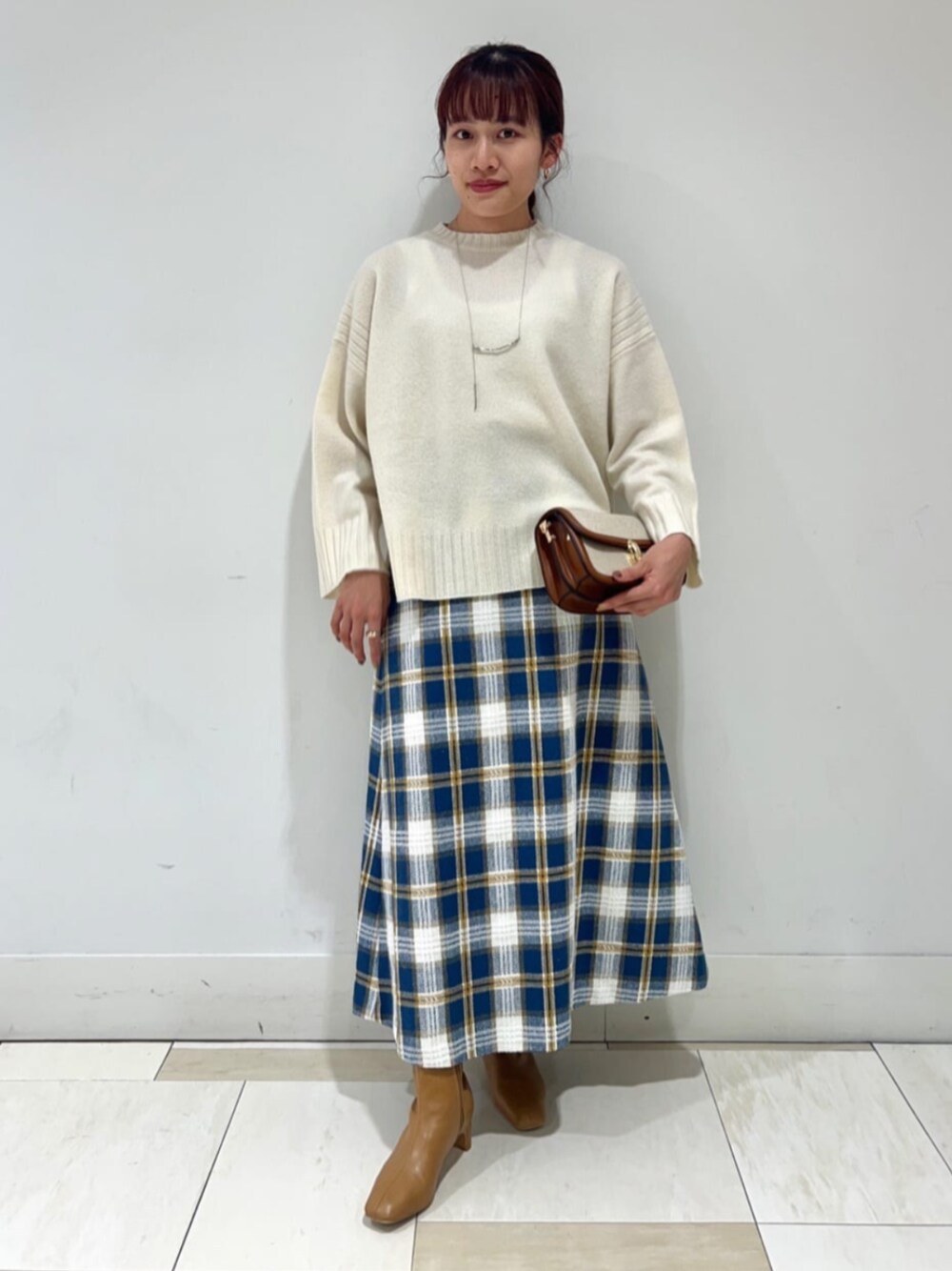 ベージュ系のブーツ、ブラウン系のビジネスバッグ、ホワイト系のニット/セーターを着用したレディースの秋コーディネートの1枚目の写真