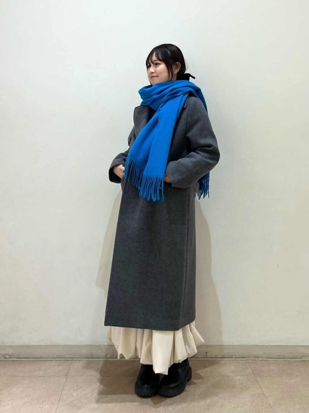 グレー系のチェスターコート、ホワイト系のスカート、ブルー系のストール/ショールを着用したレディースの冬コーディネートの1枚目の写真