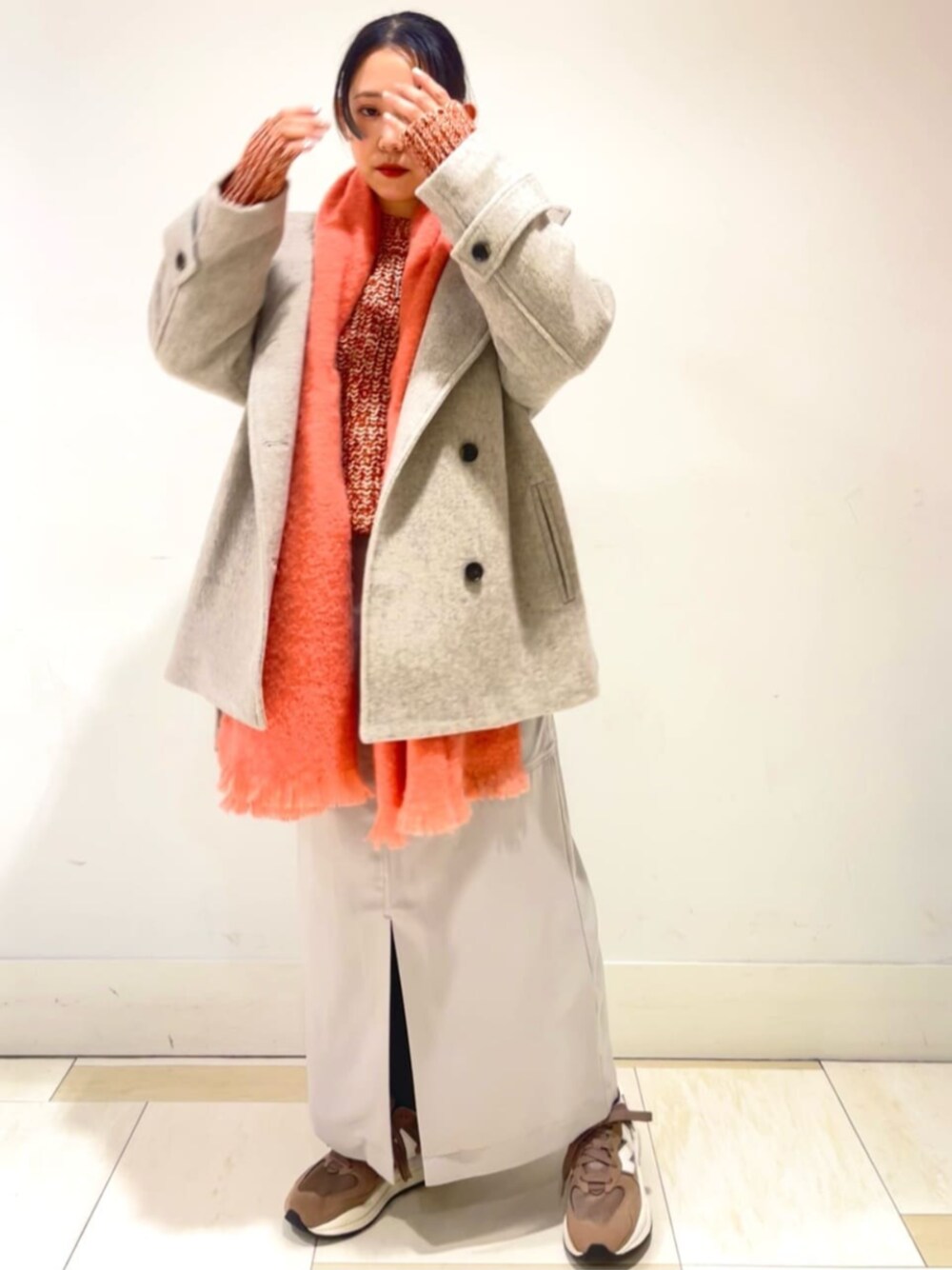 グレー系のスカート、オレンジ系のニット/セーター、ベージュ系のその他アウターを着用したレディースの冬コーディネートの1枚目の写真