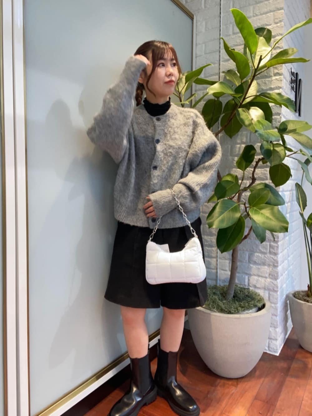 ホワイト系のビジネスバッグ、グレー系のカーディガン/ボレロ、ブラック系のブーツを着用したレディースの冬コーディネートの1枚目の写真