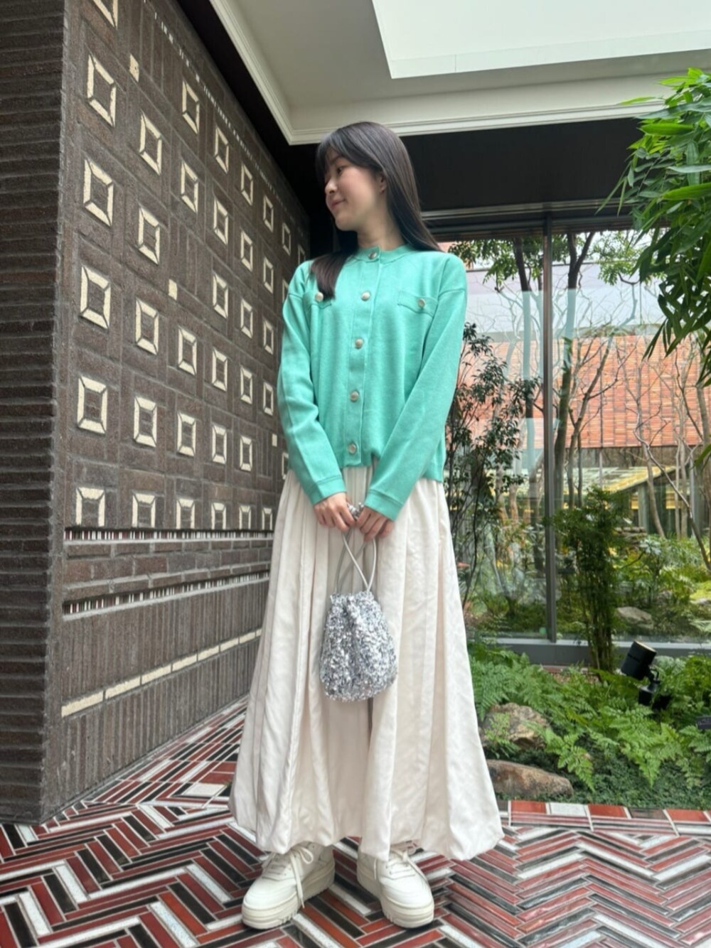 シルバー系のショルダーバッグ、グリーン系のカーディガン/ボレロ、ホワイト系のスカートを着用したレディースの冬コーディネートの1枚目の写真