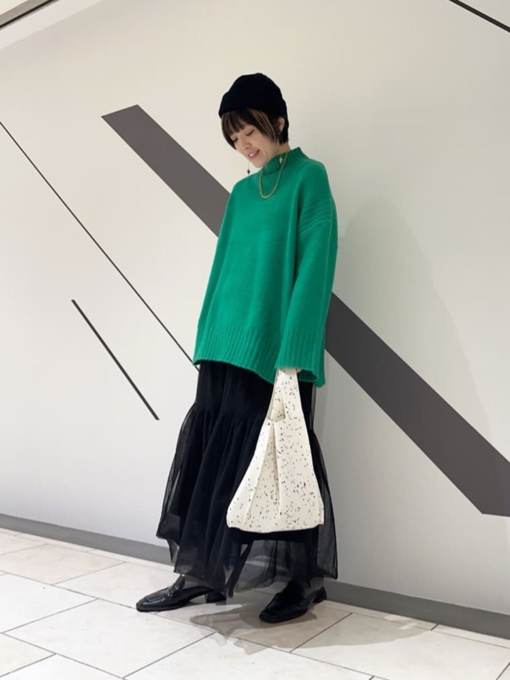 ブラック系のスカート、グリーン系のニット/セーター、ブラック系のニットキャップ/ビーニーを着用したレディースの冬コーディネートの1枚目の写真