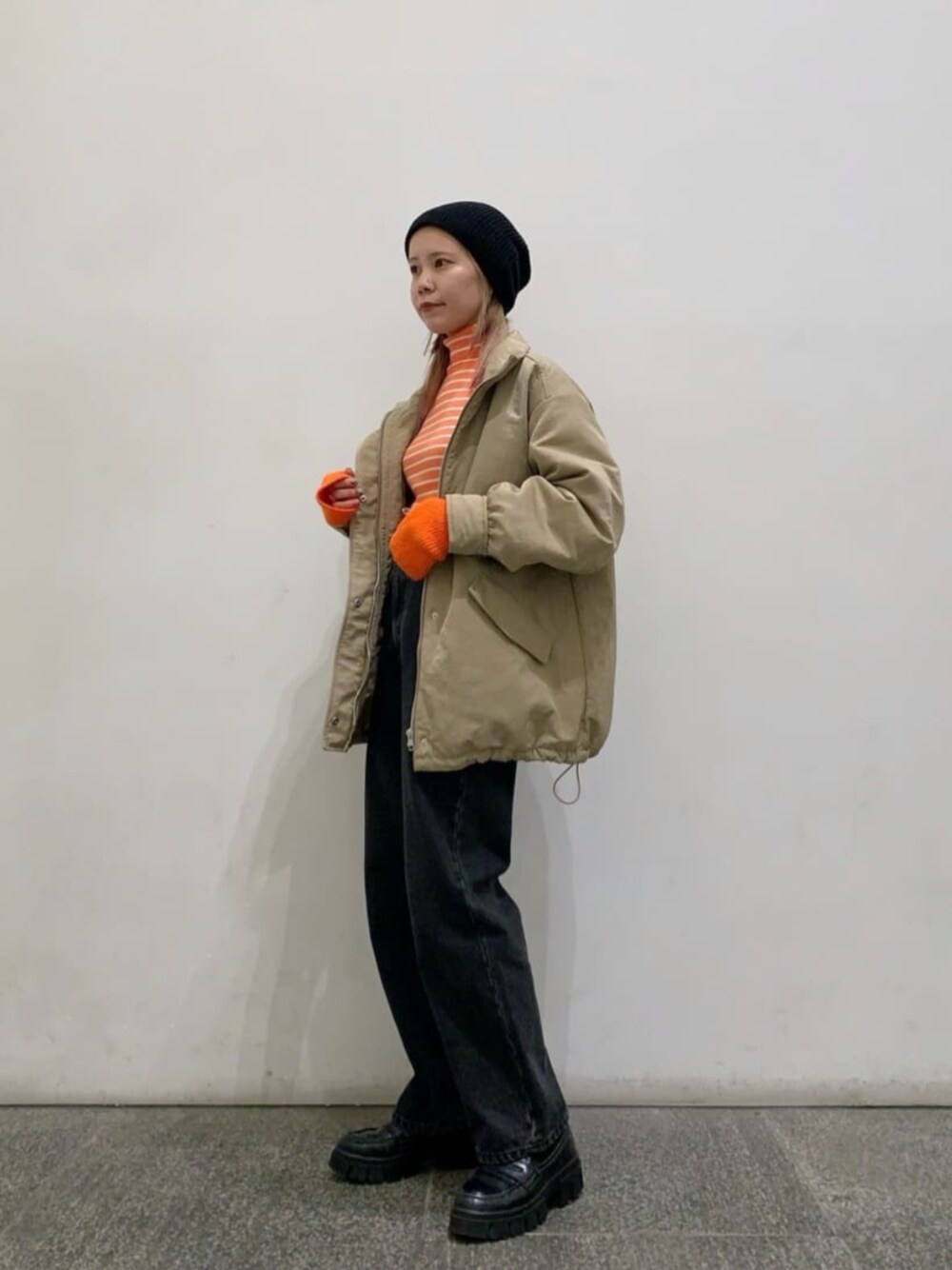 ベージュ系のブルゾン、オレンジ系のニット/セーター、ブラック系のデニムパンツを着用したレディースの冬コーディネートの1枚目の写真