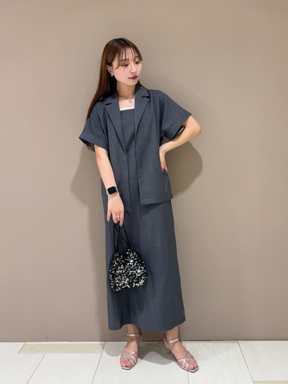 ブラック系のショルダーバッグ、シルバー系のサンダル、グレー系のワンピースを着用したレディースの春コーディネートの1枚目の写真