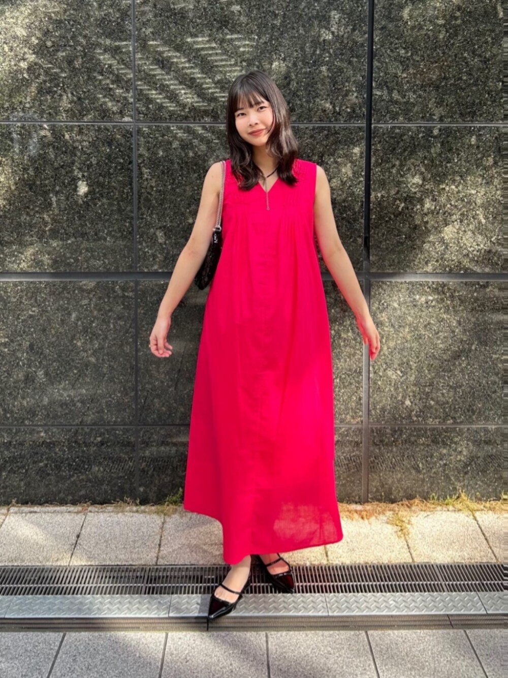 ブラック系のショルダーバッグ、ブラック系のパンプス、ピンク系のワンピースを着用したレディースの夏コーディネートの1枚目の写真