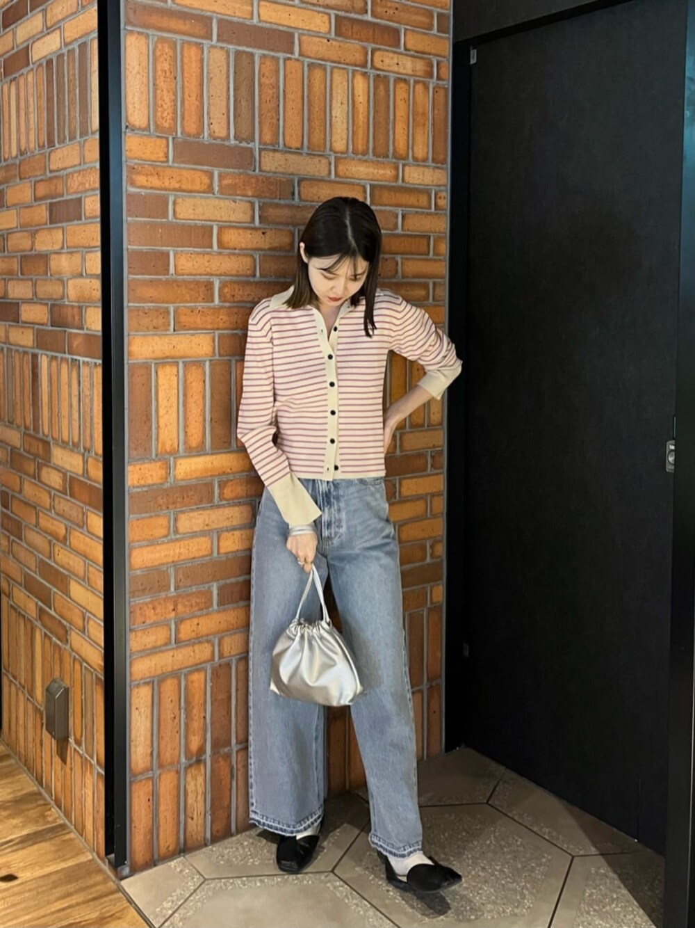 シルバー系のビジネスバッグ、ホワイト系のカーディガン/ボレロ、ブルー系のデニムパンツを着用したレディースの冬コーディネートの1枚目の写真