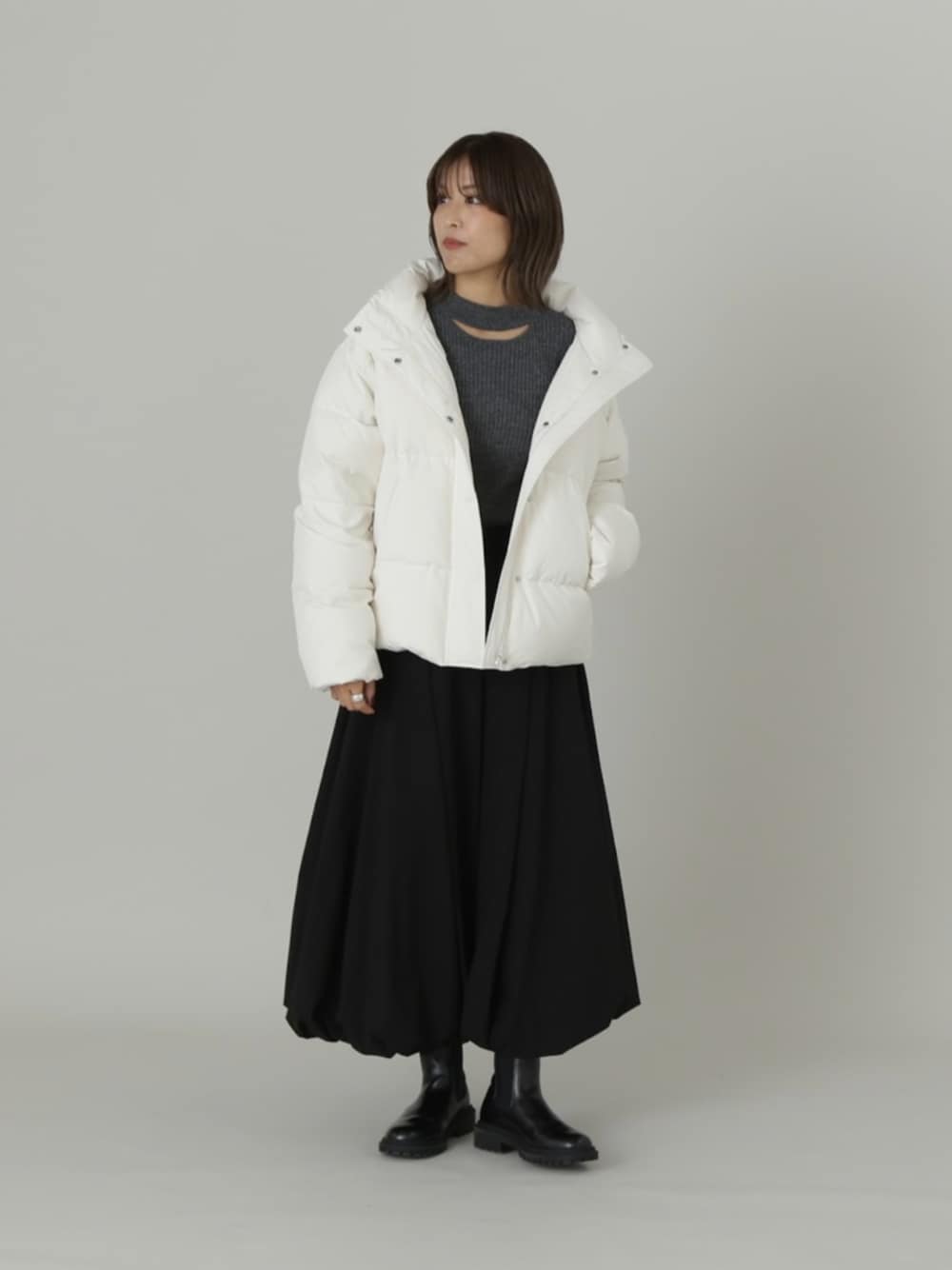 ホワイト系のダウンジャケット/コート、グレー系のニット/セーター、ブラック系のスカートを着用したレディースの秋コーディネートの1枚目の写真