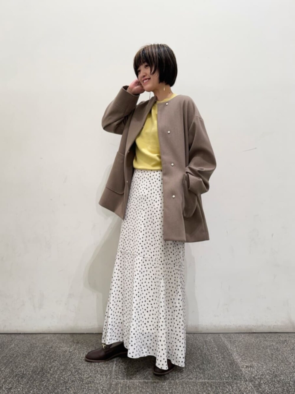 ブラウン系のノーカラーコート、イエロー系のニット/セーター、その他のスカートを着用したレディースの秋コーディネートの1枚目の写真