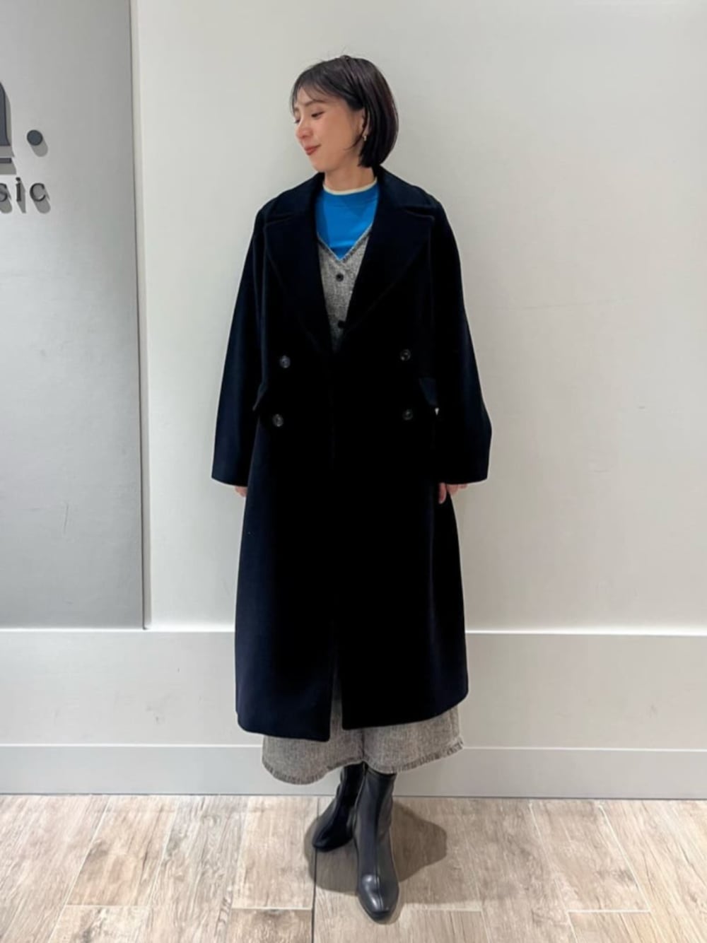 グレー系のジャンパースカート、ブルー系のニット/セーター、ブラック系のチェスターコートを着用したレディースの冬コーディネートの1枚目の写真