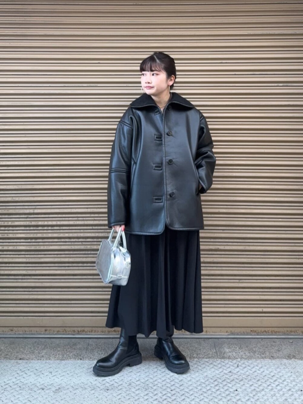 シルバー系のボストンバッグ、ブラック系のブルゾン、ブラック系のスカートを着用したレディースの冬コーディネートの1枚目の写真