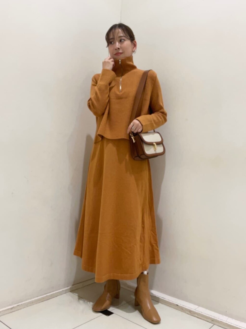 ベージュ系のブーツ、オレンジ系のワンピース、ブラウン系のビジネスバッグを着用したレディースの秋コーディネートの1枚目の写真