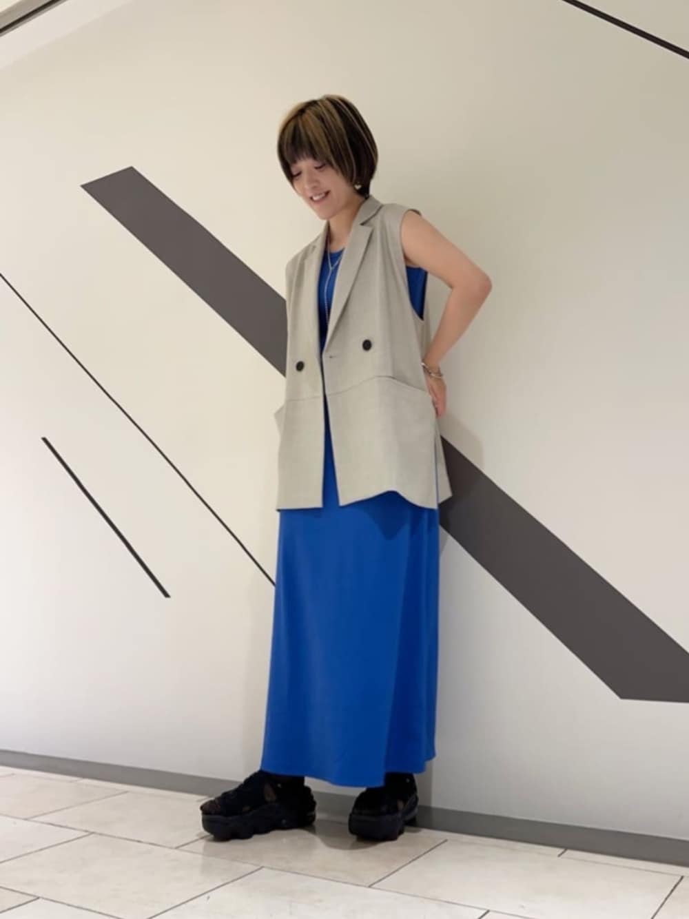 グレー系のベスト、ブルー系のワンピース、シルバー系のネックレスを着用したレディースの春コーディネートの1枚目の写真