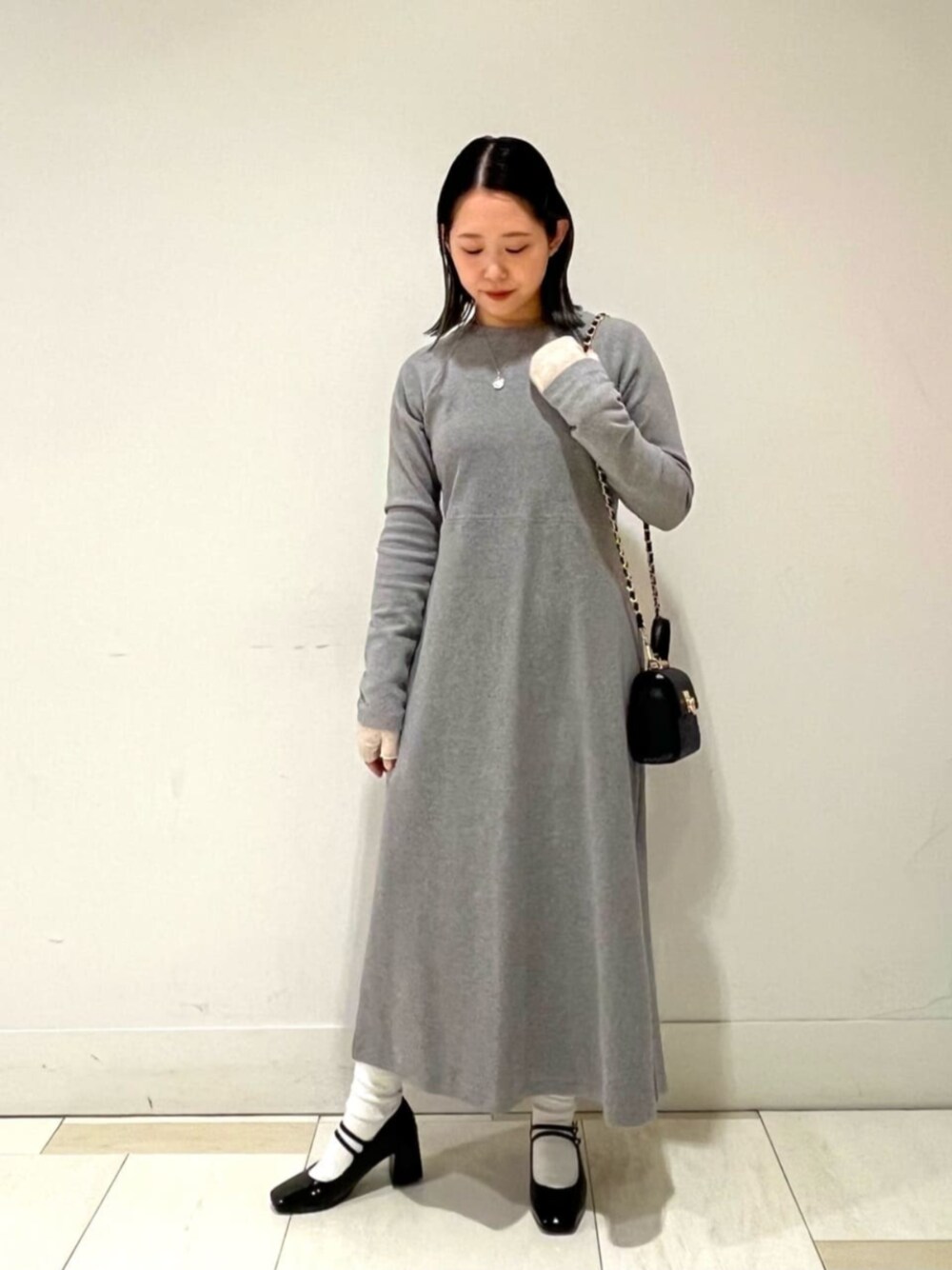 ブラック系のビジネスバッグ、ブラック系のパンプス、グレー系のワンピースを着用したレディースの冬コーディネートの1枚目の写真