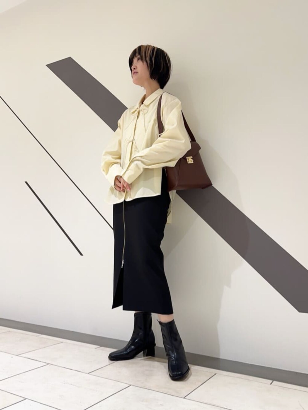 ブラウン系のショルダーバッグ、ブラック系のブーツ、ブラック系のスカートを着用したレディースの冬コーディネートの1枚目の写真