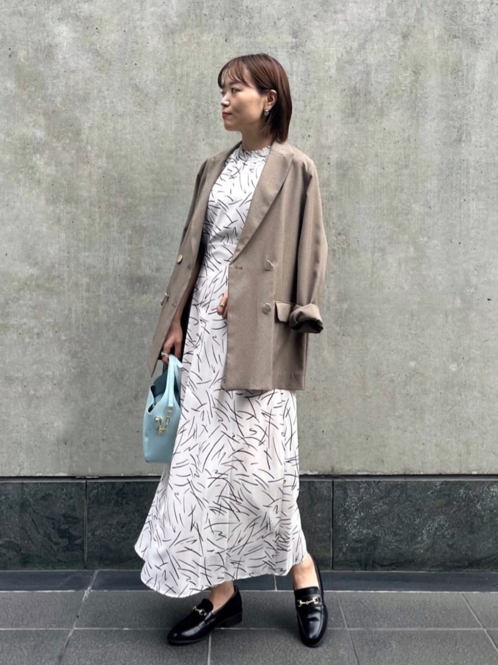 ブラック系のローファー、ホワイト系のワンピース、ブラウン系のテーラードジャケットを着用したレディースの夏コーディネートの1枚目の写真