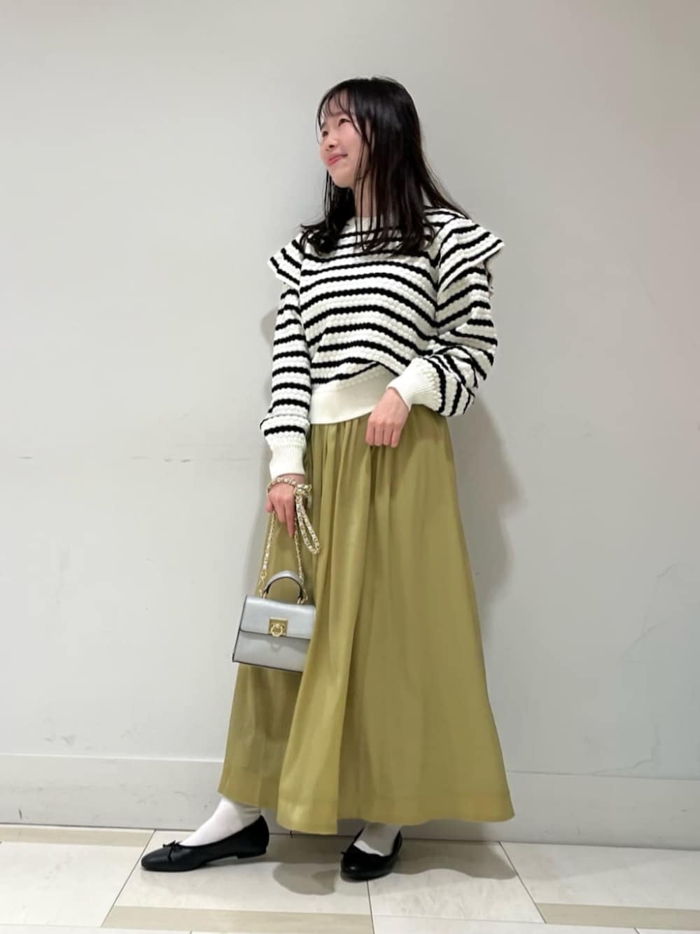 シルバー系のビジネスバッグ、ホワイト系のニット/セーター、イエロー系のスカートを着用したレディースの冬コーディネートの1枚目の写真