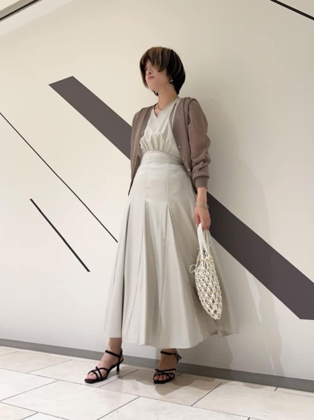 ブラック系のサンダル、ホワイト系のショルダーバッグ、ベージュ系のワンピースを着用したレディースの春コーディネートの1枚目の写真