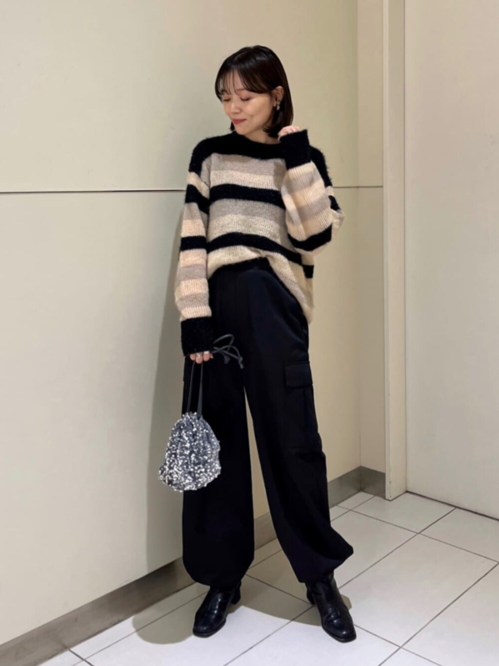 グレー系のビジネスバッグ、ブラック系のブーツ、ブラック系のニット/セーターを着用したレディースの秋コーディネートの1枚目の写真