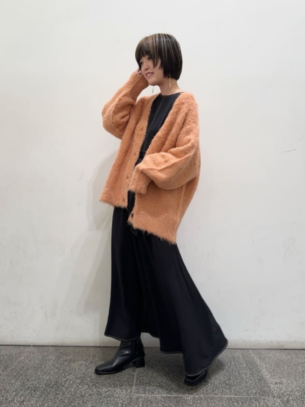 ブラック系のブーツ、オレンジ系のカーディガン/ボレロ、ブラック系のワンピースを着用したレディースの秋コーディネートの1枚目の写真