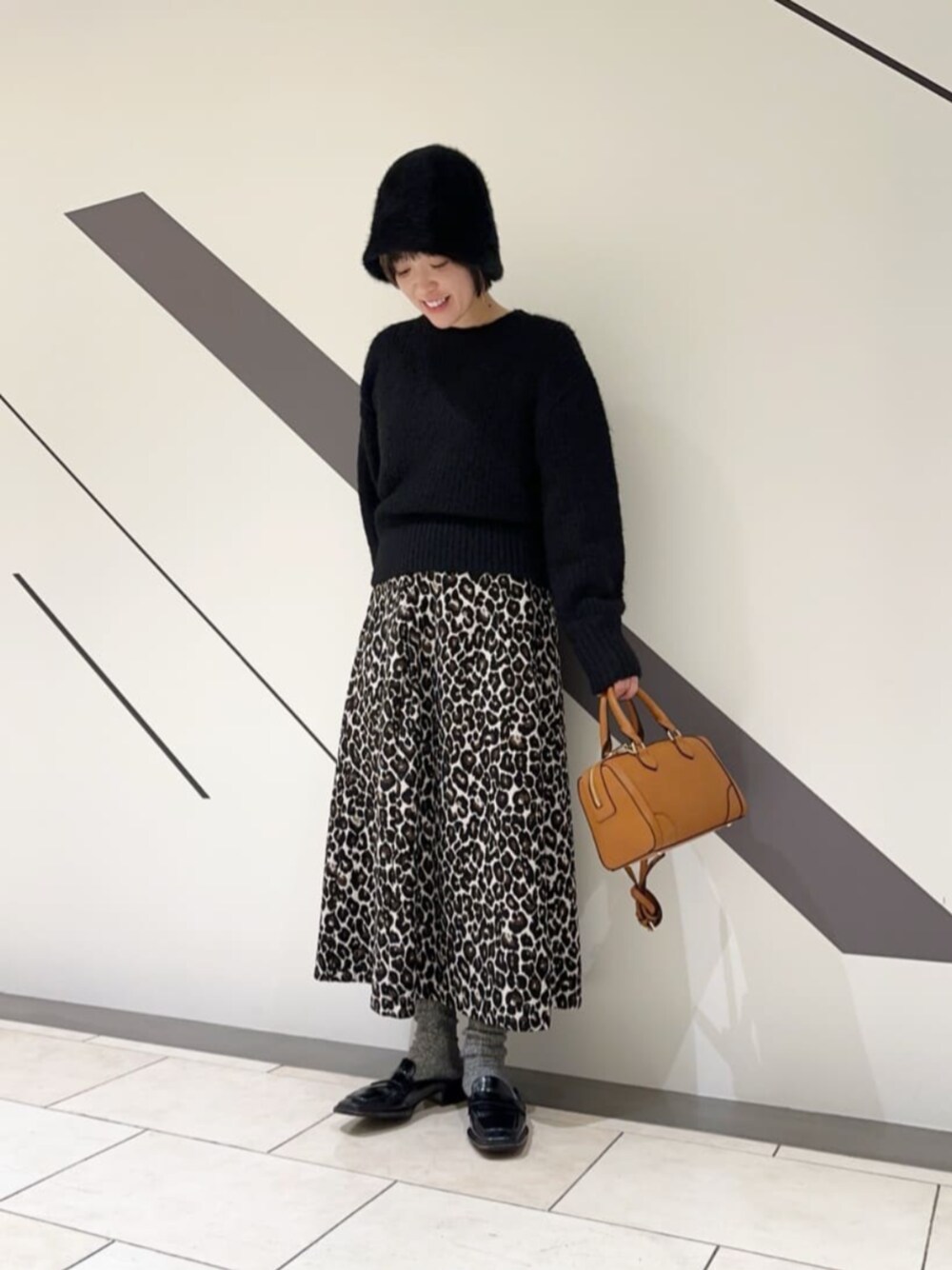 ブラウン系のトートバッグ、ブラック系のニット/セーター、ホワイト系のスカートを着用したレディースの冬コーディネートの1枚目の写真