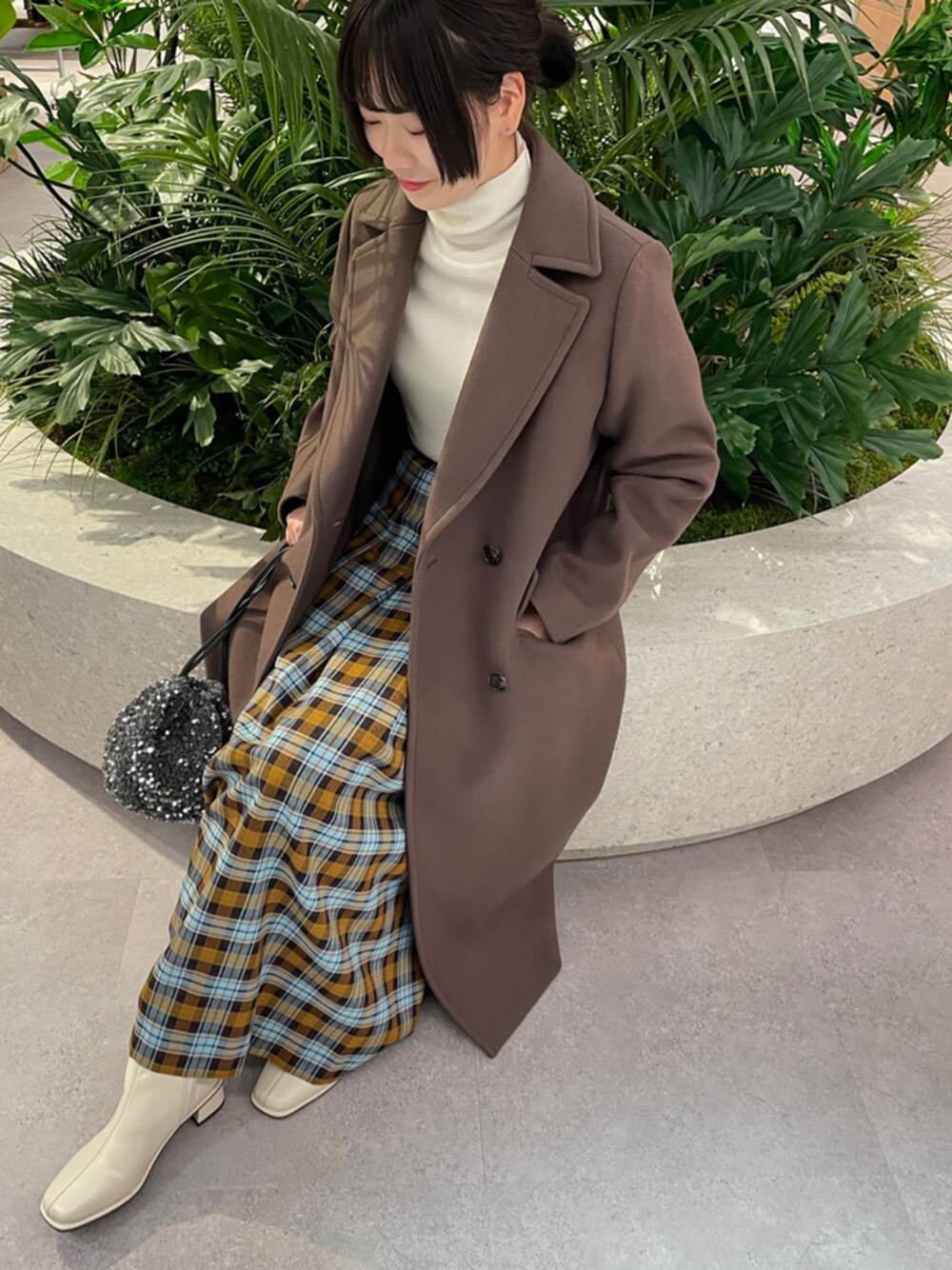 グレー系のビジネスバッグ、ホワイト系のブーツ、イエロー系のスカートを着用したレディースの秋コーディネートの1枚目の写真