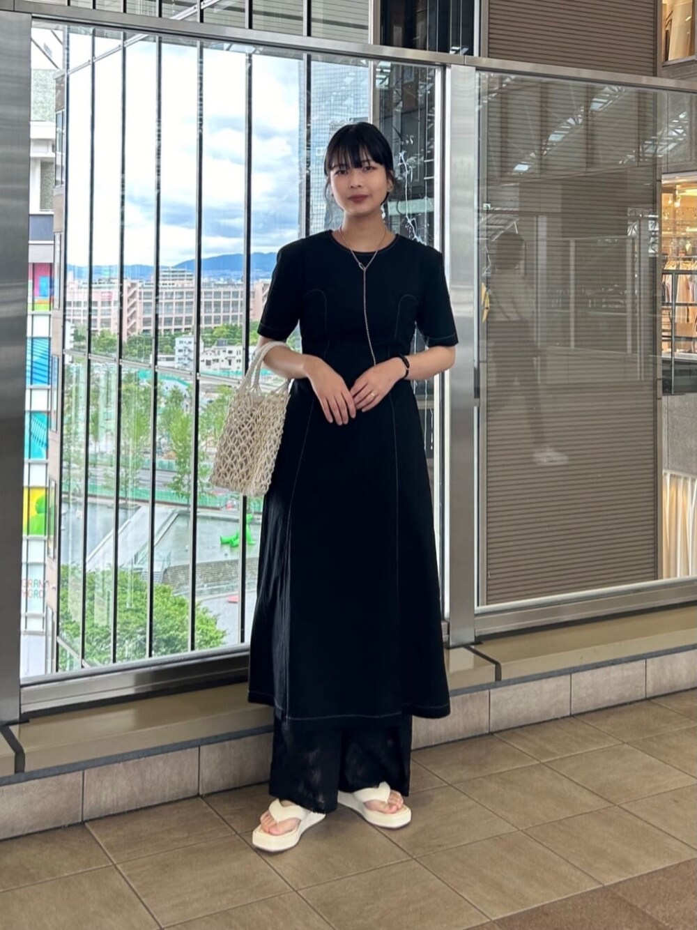 ホワイト系のショルダーバッグ、ホワイト系のサンダル、ブラック系のワンピースを着用したレディースの春コーディネートの1枚目の写真