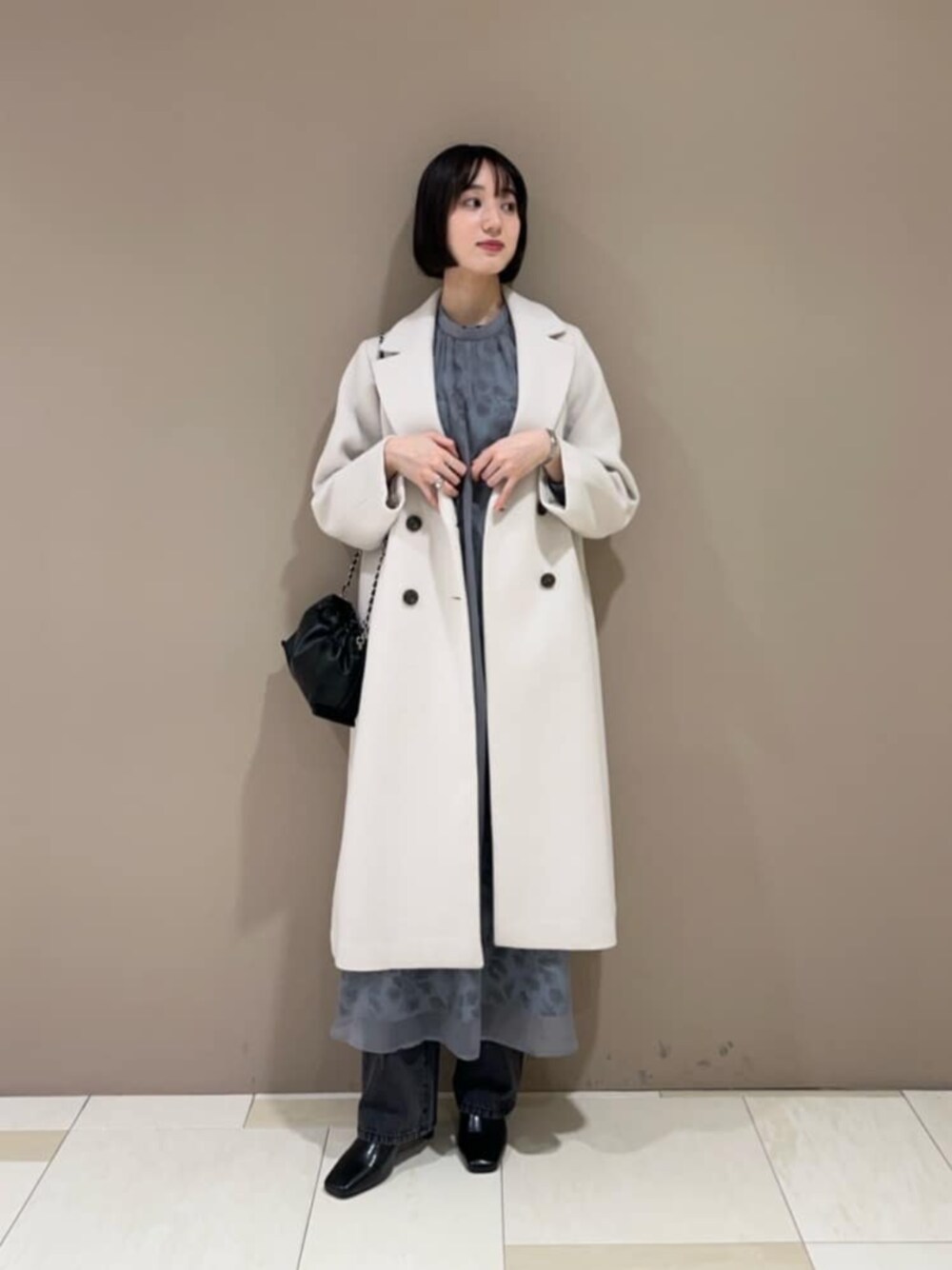 ブラック系のデニムパンツ、ブルー系のワンピース、ホワイト系のチェスターコートを着用したレディースの冬コーディネートの1枚目の写真