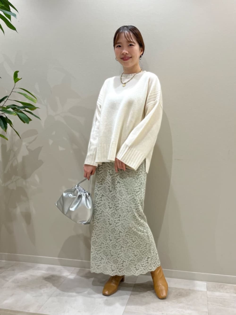 ベージュ系のブーツ、シルバー系のビジネスバッグ、ホワイト系のニット/セーターを着用したレディースの秋コーディネートの1枚目の写真